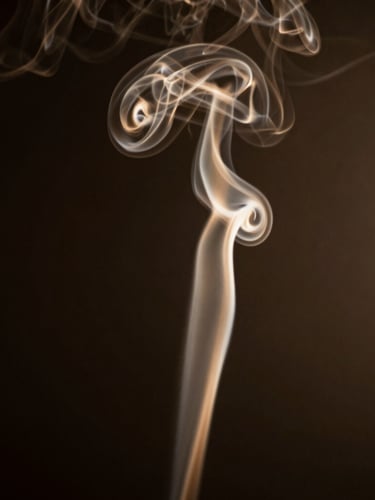 Elegant silhouette of rising smoke curls against a dark, low-key background with warm golden undertones, dramatic side-lighting.