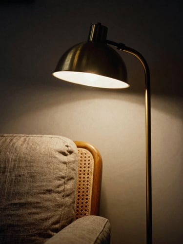 Moody architectural photography, close-up of a curved floor reading lamp casting a warm pool of light onto a linen armchair, deep shadows, rich unlacquered brass texture, medium format film.