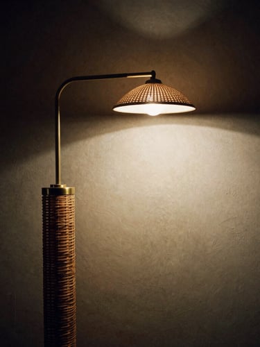 Moody architectural photography of a curved brass floor reading lamp casting a warm pool of light onto a textured plaster wall, medium format film, deep shadows.