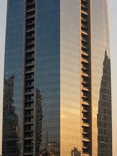 Architectural detail of modern financial district skyscraper in Riyadh, sharp geometric shadows, clean glass and steel lines against a warm golden-hour sky.