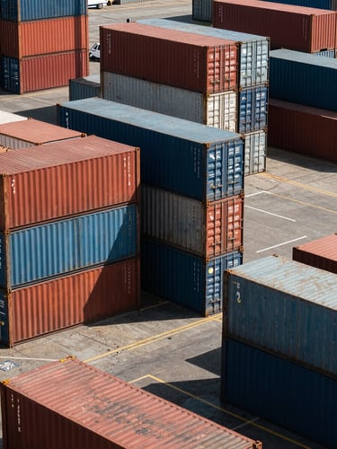 A wide-angle, high-contrast shot of stacked shipping containers at a busy West African port, harsh direct sunlight casting deep geometric shadows, industrial scale.