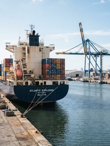 Wide-angle commercial cargo vessel docked at a harbor during bright daylight, clean slate blue water, industrial crane in the background, sharp focus, 35mm