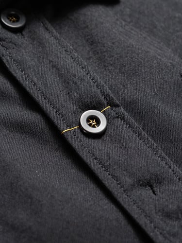 Extreme macro close-up of precise gold embroidery thread on a heavy matte charcoal oxford cotton shirt, dramatic studio side lighting, shallow depth of field showing fabric weave.