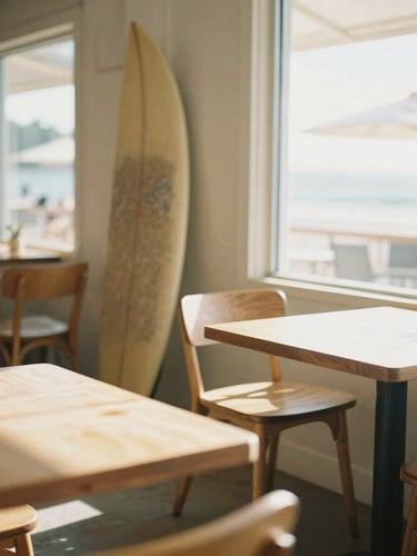 Bright sunlit cafe interior with light wood tables, a vintage surfboard leaning in the corner, and warm daylight streaming through large windows, 35mm photography