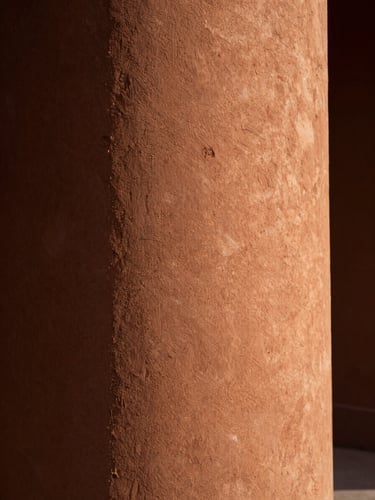 Close-up of a textured terracotta wall with raking warm light from the right edge, deep shadow to the left, architectural surface detail, cinematic stillness, no people
