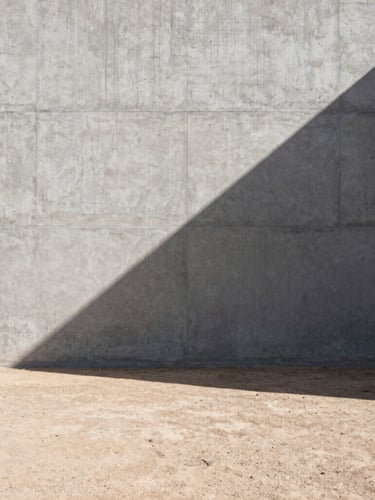 Stark architectural photography of a raw concrete wall casting a sharp geometric shadow across a dry desert floor, harsh direct sunlight, wide-angle lens