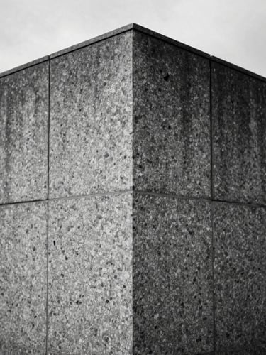 Straight-on architectural elevation of a monolithic granite wall, sharp joint lines, raking side-light highlighting the hand-chiseled texture, overcast daylight, desaturated slate tones.