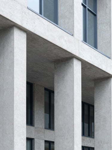 Crisp architectural crop of a modern civic building with concrete pillars, bright neutral daylight, clean lines, desaturated corporate blues, high detail, 35mm