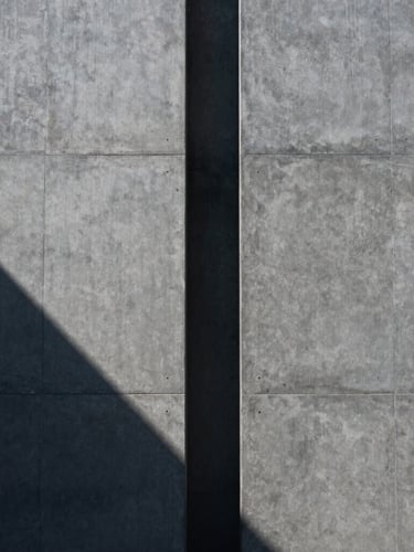 Symmetrical architectural concrete facade with sharp diagonal shadows, cool daylight, minimalist composition, 35mm lens