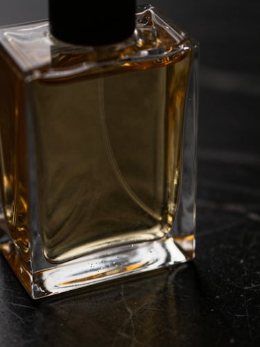 Extreme close-up of a heavy glass perfume bottle reflecting golden light on a dark marble surface, dramatic chiaroscuro lighting, shallow depth of field