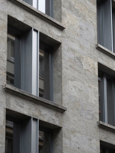 Abstract architectural detail of a renovated historic stone facade in Lausanne, showing the contrast between clean modern metal window frames and textured grey stone, soft northern light.