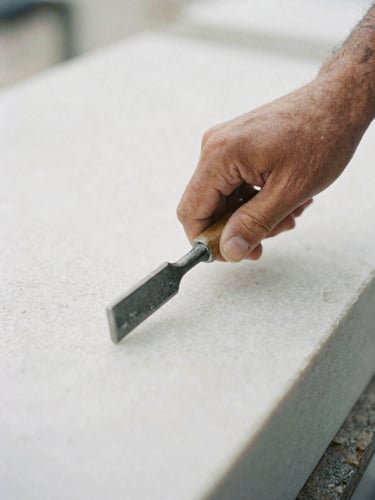 Close-up of a master stonemason's hand guiding a chisel on a raw white marble block, soft overcast daylight, shallow depth of field, 35mm film texture