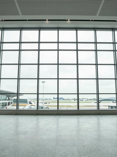 Symmetrical wide-angle shot of a modern glass-and-steel airport terminal interior, bright overcast daylight streaming through high windows, cool slate tones, sharp focus.