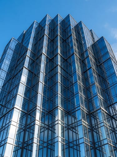 Wide shot of a modern glass-clad skyscraper facade reflecting a clear blue sky, sharp architectural lines, bright morning light, no streaks or imperfections.