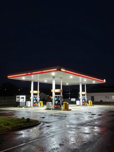 Wide shot of a high-canopy fuel station along the Bedford A421 corridor at night, bright white security lights illuminating the empty forecourt, wet asphalt reflecting the light.