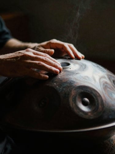 Close-up of hands gently striking a dark metallic handpan, soft dramatic side-lighting, dust particles floating in a single beam of light, shallow depth of field, 35mm film style