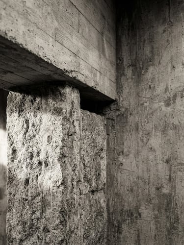 Tight off-center monochrome architectural close-up of stone pillars meeting concrete beams, dramatic side lighting, textured brush background, desaturated warm tones, medium format film.