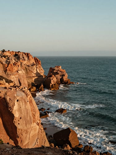 Vue verticale de la côte sauvage de Tanger, falaises de grès ocre plongeant dans l'océan Atlantique, lumière vive de fin d'après-midi, cadrage artistique minimaliste.
