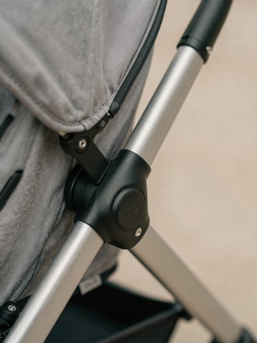 Macro detail shot of a stroller's reinforced mechanical folding joint, brushed steel and matte black finish, clean technical lines, soft daylight, 35mm