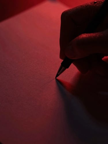 High-contrast low-key close-up of hands writing on dark paper, dramatic side-lighting casting deep shadows, crimson tones, macro lens
