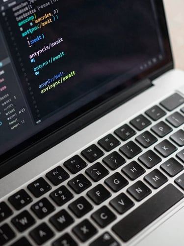 Extreme close-up overhead view of a laptop keyboard with a code editor open showing JavaScript syntax — async/await functions highlighted in teal on a dark terminal, clean studio lighting, no people