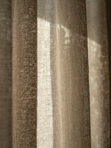 Macro detail shot of heavy oatmeal linen drapery catching dramatic raking window light, showing dense weave texture, warm desaturated earth tones, 35mm.
