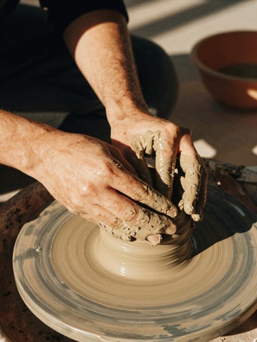 Warm, medium close-up of hands molding clay together in an intergenerational workshop, golden-hour light, rich textures, 35mm film.