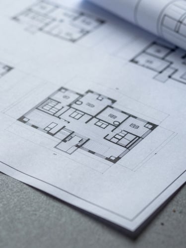 Macro close-up of physical architectural blueprints and digital wireframes on a slate gray desk, minimal shadows, clean studio lighting, cool overcast daylight, 35mm