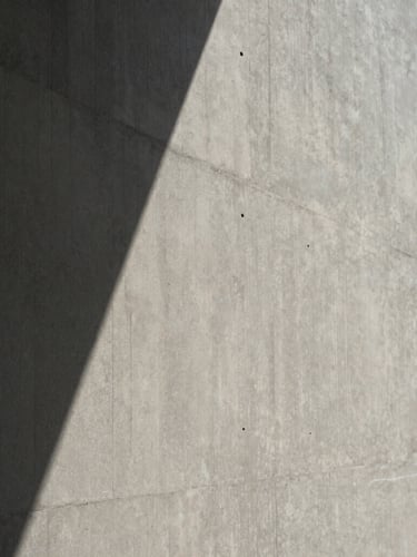 Close-up of a textured concrete wall with sharp geometric shadows from direct sunlight, minimalist architectural aesthetic, desaturated neutral tones, 35mm lens.
