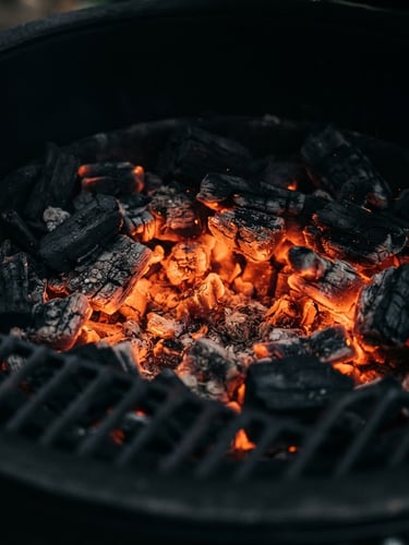 Moody close-up of glowing orange embers inside a sleek matte-black grill, low-key lighting, deep shadows, high contrast