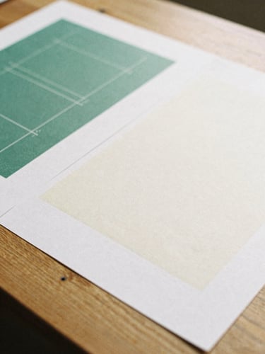 Close-up of physical design proofs on a heavy oak table, soft overcast British daylight, muted forest green and warm cream tones, 35mm film grain