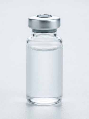 Extreme close-up macro photography of a sealed glass vial containing clear liquid, sitting on a sterile white laboratory surface, bright diffused cool studio lighting, 100mm macro lens.