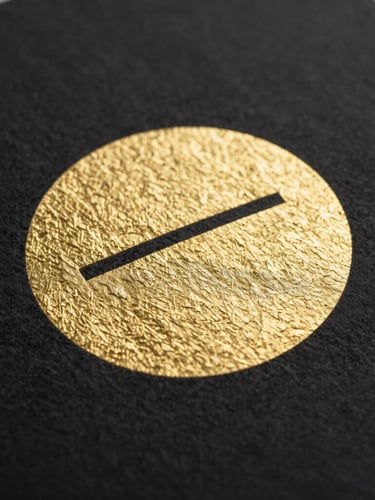 Close-up of embossed gold foil on heavy black cardstock, tactile paper texture, macro studio photography, sharp focus