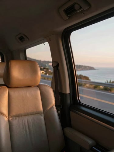 A passenger perspective looking out of a clean private transfer car window at golden hour, soft light hitting the leather interior, scenic coastal road visible outside.