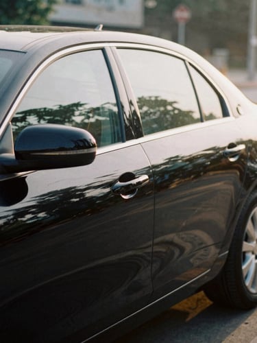 A sleek private black car waiting at the curb in soft morning daylight, passenger luggage handle visible, documentary travel photography, 35mm.