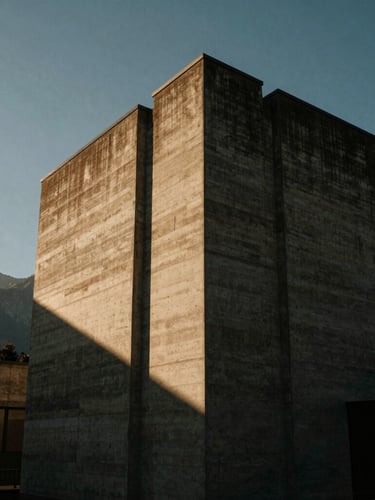 A tall portrait crop of Villa Noire's concrete cantilevered corner, dramatic low-angle sunlight casting sharp diagonal shadows, mountains in the soft background.