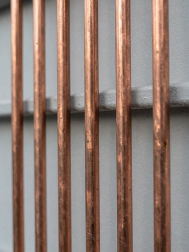 Macro shot of perfectly aligned clean copper pipes on a light gray industrial wall, bright neutral daylight, technical precision.