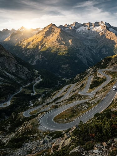 Wide-angle view of a winding mountain road with multiple hairpins, possibly Stelvio or Furka Pass, under dramatic dawn light with deep shadows, a small campervan visible in the distance, emphasizing immense scale.