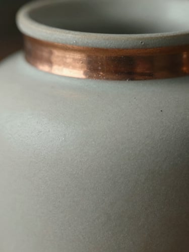 Close-up macro shot of matte ceramic texture and brushed-copper accent details, soft directional natural light.
