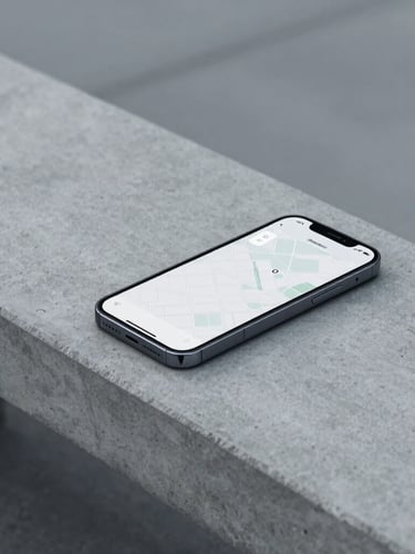 A close-up of a modern smartphone resting on a clean concrete bench, displaying a minimalist interface with a map outline, cool overcast daylight, desaturated navy and gray tones, 35mm.
