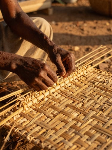 A close-up portrait of local artisan hands weaving a traditional straw mat on Azizakpe Island, warm golden-hour sunlight filtering through, rich saturated earth tones, 35mm editorial.