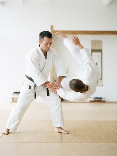 Bright minimalist photography of two adult aikido practitioners in white keikogi executing a fluid throw, soft natural dojo light, clean white background, subtle cobalt blue accents, 35mm