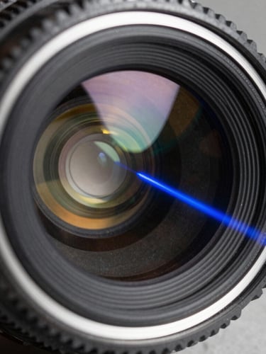 Macro shot of a multi-element optical lens catching a sharp blue laser beam, showing internal refraction paths and high-contrast glass edges.