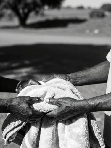 Dignified close-up of South African community volunteer handing a warm blanket to an elder, natural high-contrast afternoon sunlight, 35mm lens