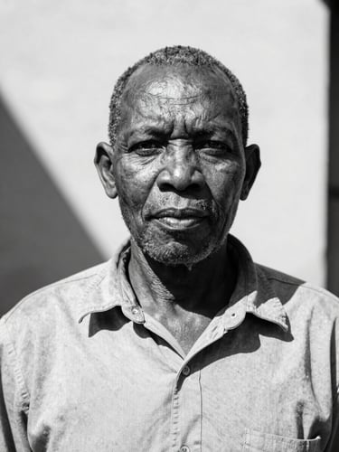 Dignified eye-level portrait of a South African community leader in natural high-contrast sunlight, crisp black and white tones, deep shadows, 35mm lens