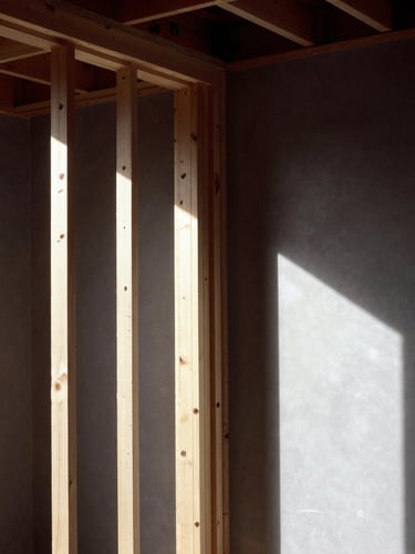 Architectural interior under construction, crisp wood framing studs visible on one side transitioning to finished smooth drywall on the other, dramatic raking light, high contrast