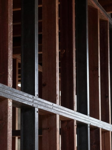 Raw geometric timber and steel wall framing under high-contrast dramatic raking light, sharp focus, architectural precision.