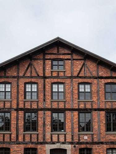 Straight-on architectural elevation of a restored brick and timber building, clean overcast daylight, sharp structural lines, negative space above.