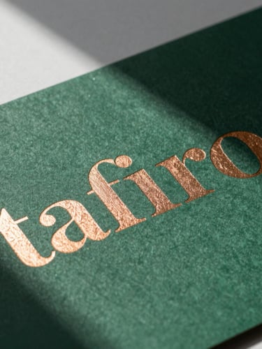 Extreme close-up of high-contrast directional studio lighting casting sharp shadows on printed brand collateral, textured forest green paper with debossed copper foil typography, clean workspace background.