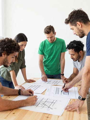 A bright environmental photo of a community planning workshop, people looking at architectural blueprints on a wooden table, natural daylight, 35mm.